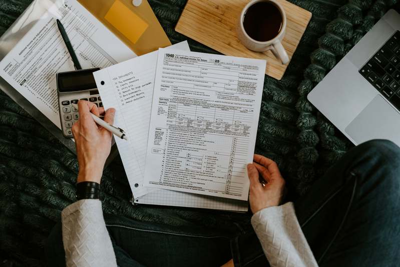 Close-up of hands using a pen to write 'Monthly Budget' in a lined notebook beside a smartphone showing a budgeting app